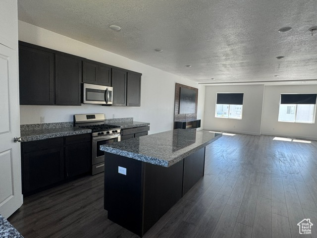 Kitchen with appliances with stainless steel finishes, dark cabinetry, a kitchen island, a textured ceiling, and dark wood-type flooring