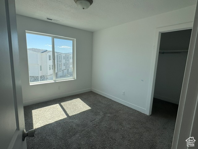 Unfurnished bedroom with dark colored carpet, a textured ceiling, a spacious closet, a closet, and baseboards
