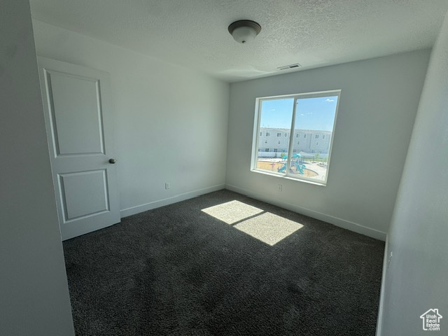Spare room with dark carpet, a textured ceiling, and baseboards