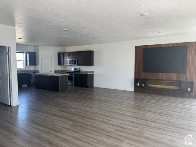 Kitchen with stainless steel appliances, a textured ceiling, a kitchen island, open floor plan, and dark wood-type flooring