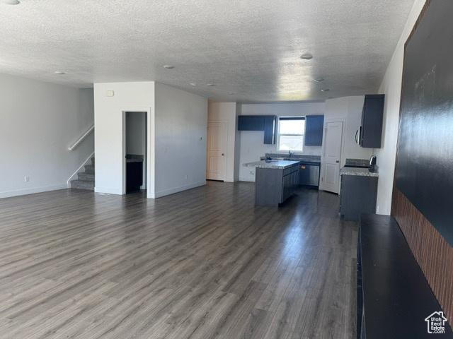 Unfurnished living room with a textured ceiling, stairway, dark wood-style floors, a sink, and baseboards
