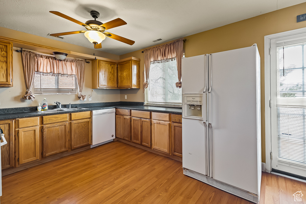 Kitchen with white appliances, brown cabinetry, a sink, light wood-style flooring, and a ceiling fan
