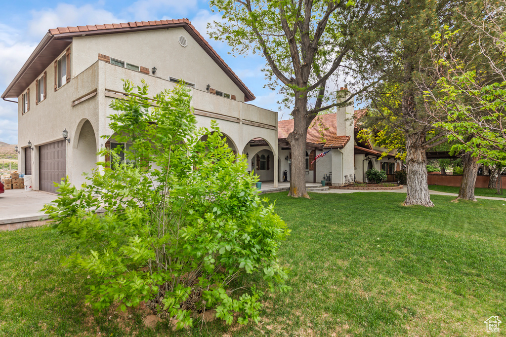 Rear view of house featuring stucco siding, a lawn, a tiled roof, a balcony, and a garage