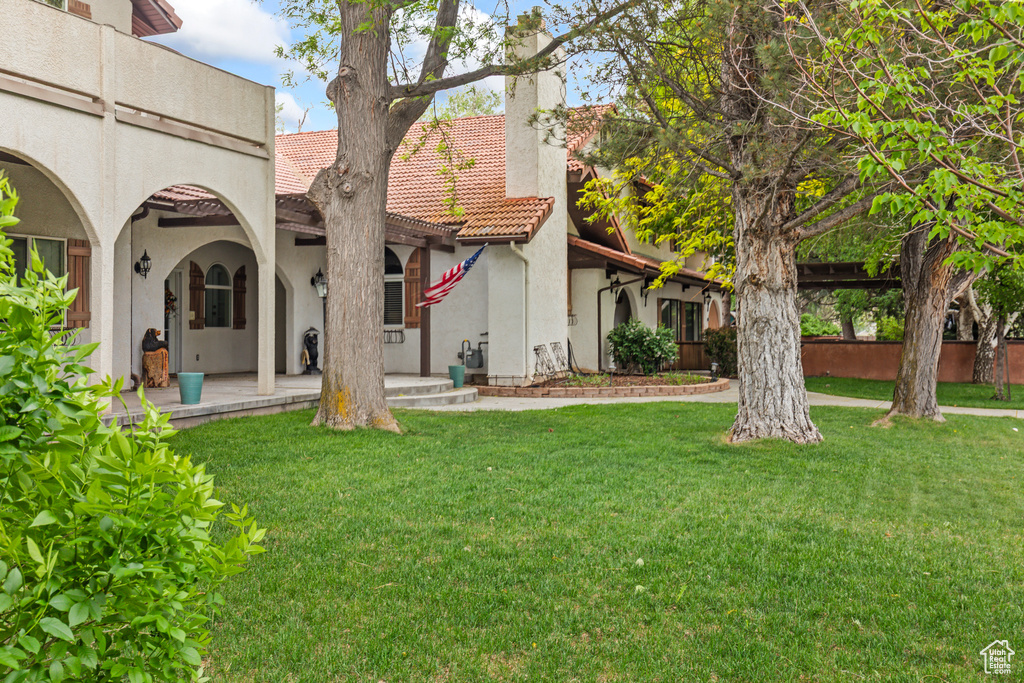 Rear view of house with stucco siding, a chimney, a lawn, and a tile roof