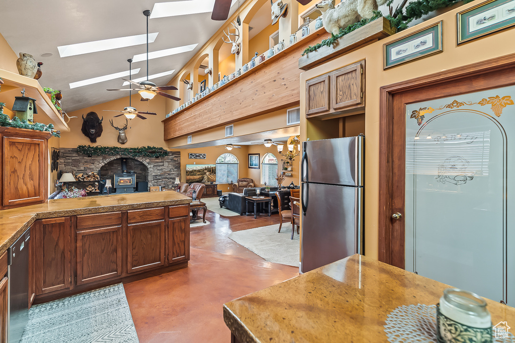 Kitchen with appliances with stainless steel finishes, ceiling fan, a skylight, finished concrete floors, and a fireplace