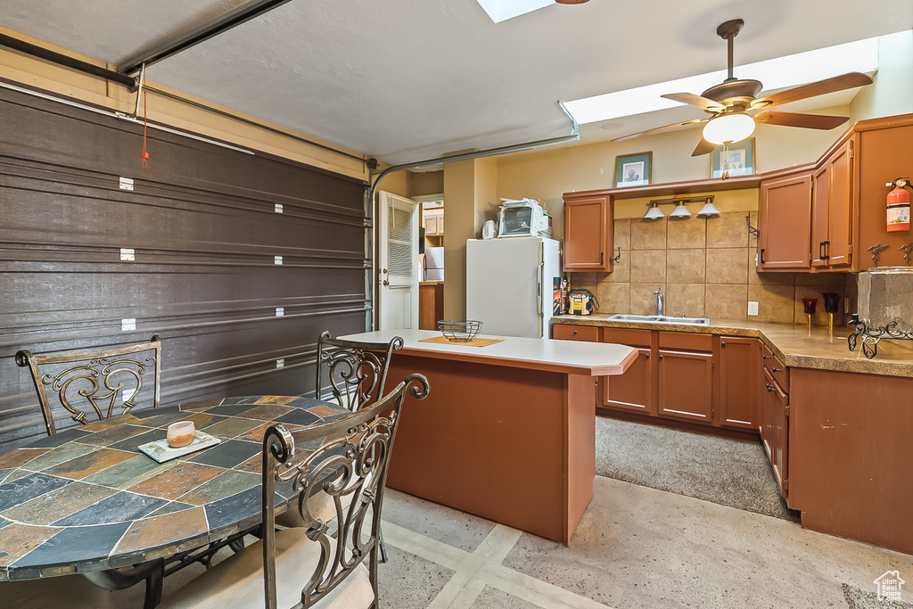 Kitchen featuring freestanding refrigerator, a sink, decorative backsplash, light countertops, and a ceiling fan