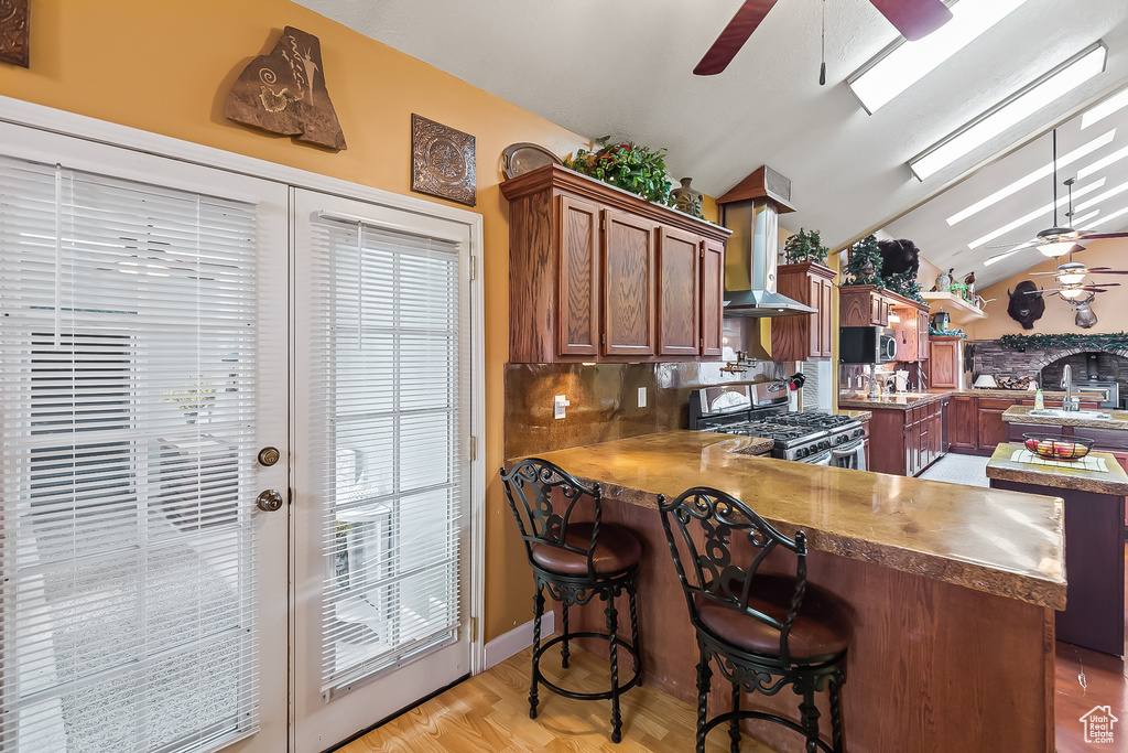 Kitchen featuring stainless steel appliances, a ceiling fan, wall chimney exhaust hood, a peninsula, and vaulted ceiling