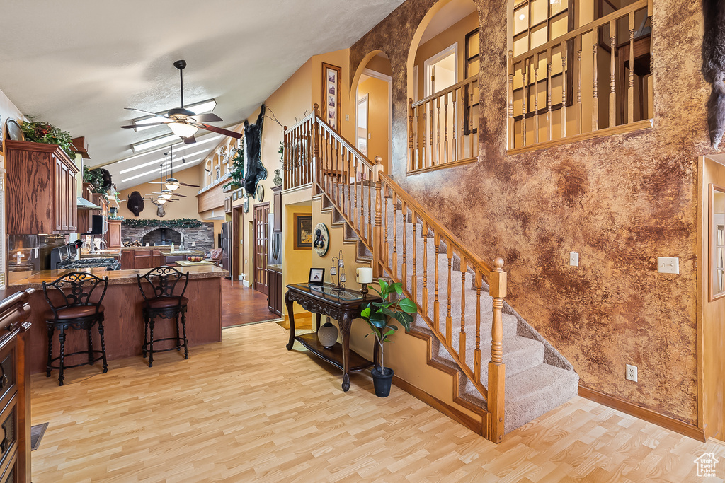 Staircase with wood finished floors, a ceiling fan, arched walkways, high vaulted ceiling, and baseboards