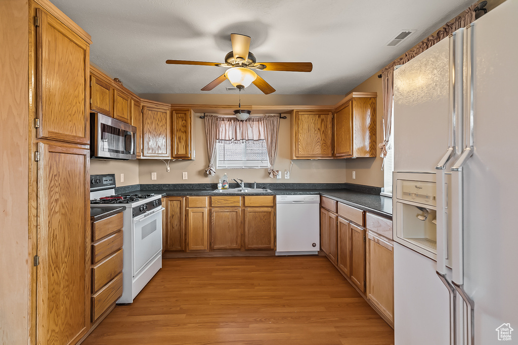 Kitchen with white appliances, a sink, dark countertops, light wood-type flooring, and ceiling fan