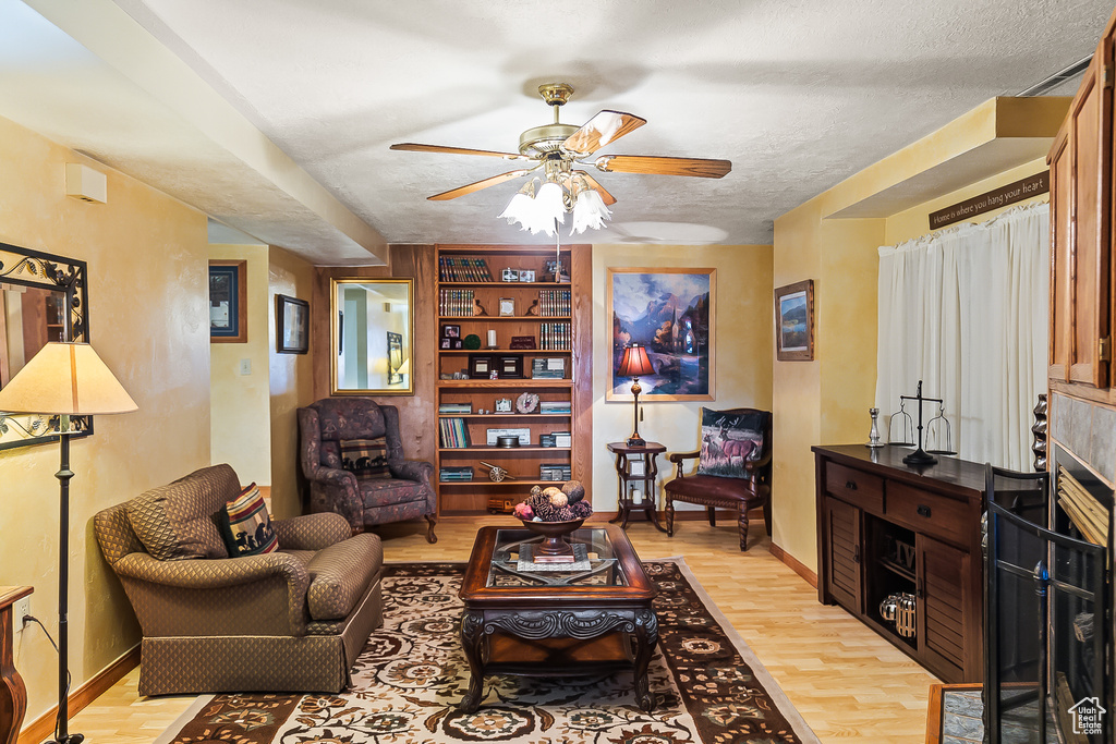 Living room with ceiling fan, light wood-style flooring, baseboards, and a textured ceiling