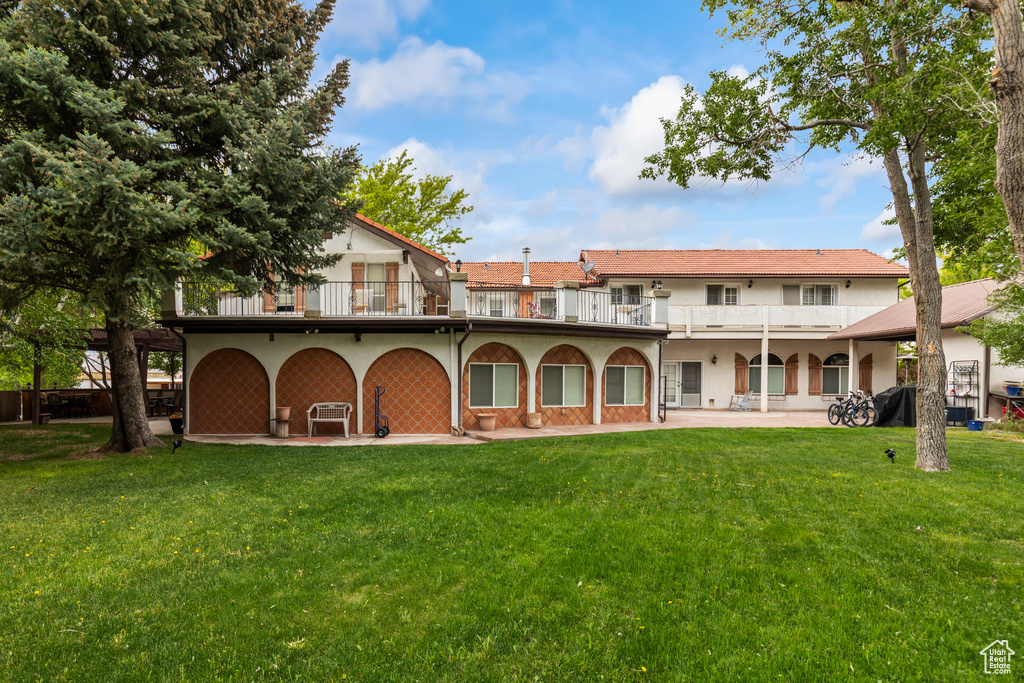 Back of house with a balcony, a yard, stucco siding, and a patio