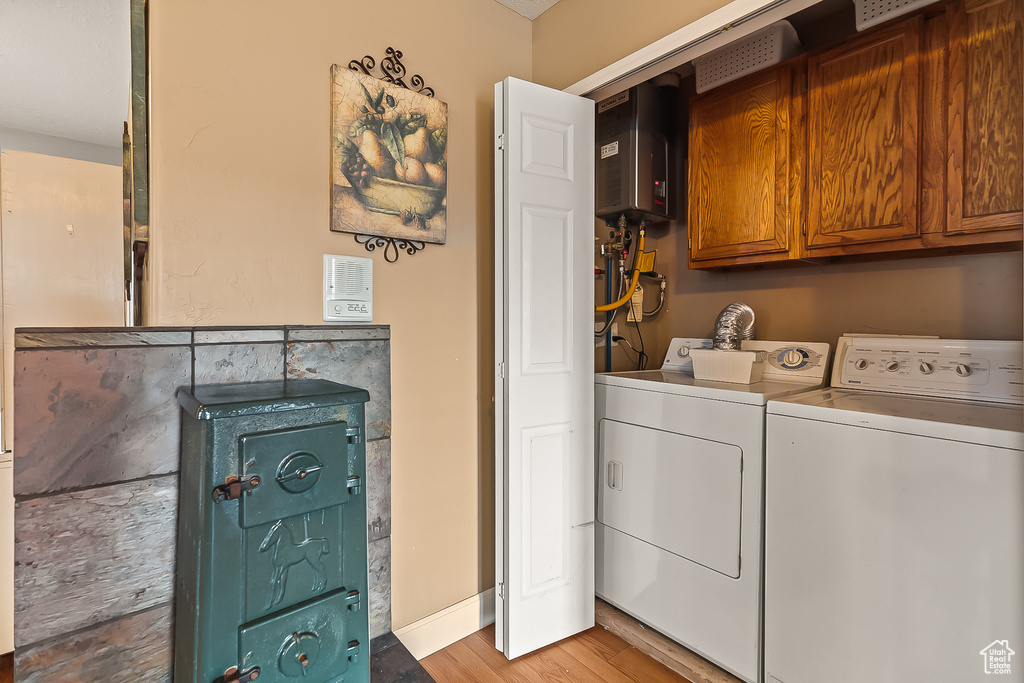 Laundry room with washer and dryer, light wood-style flooring, cabinet space, water heater, and baseboards