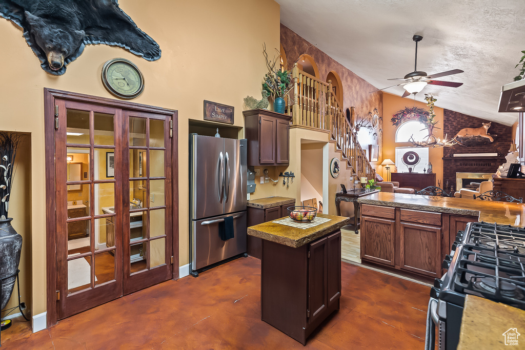 Kitchen featuring freestanding refrigerator, lofted ceiling, range with gas stovetop, a ceiling fan, and a brick fireplace