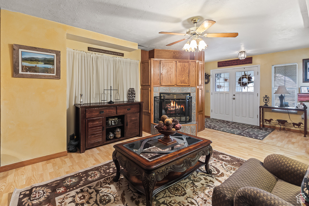 Living area featuring light wood-style floors, a ceiling fan, a warm lit fireplace, and baseboards