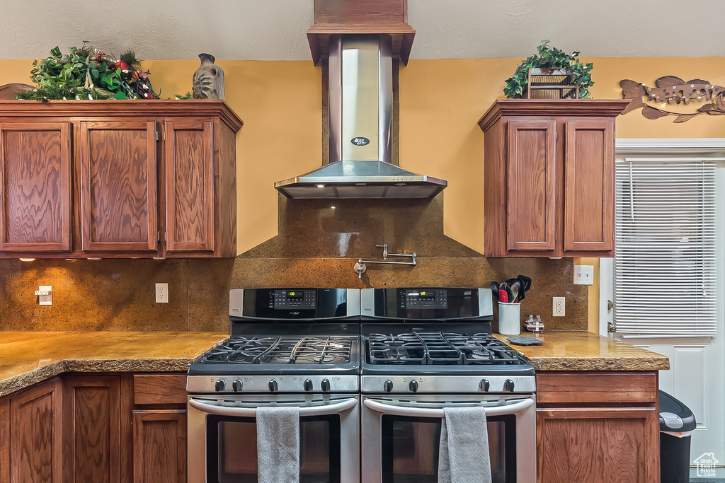 Kitchen with stainless steel gas range oven, extractor fan, backsplash, and brown cabinetry