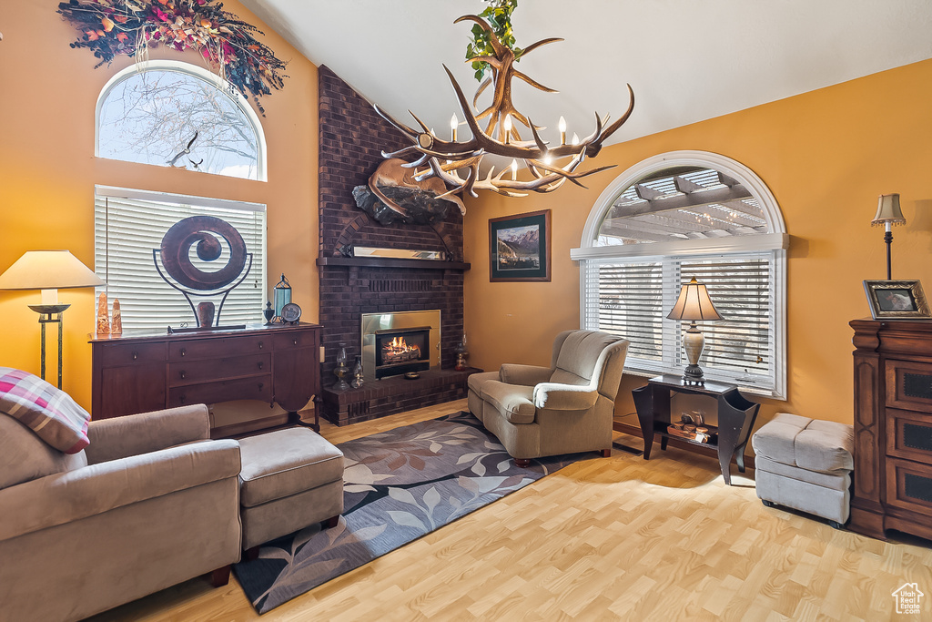 Living area featuring a chandelier, high vaulted ceiling, wood finished floors, and a brick fireplace