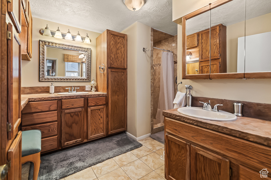 Full bath featuring tiled shower, a textured ceiling, tile patterned floors, and two vanities