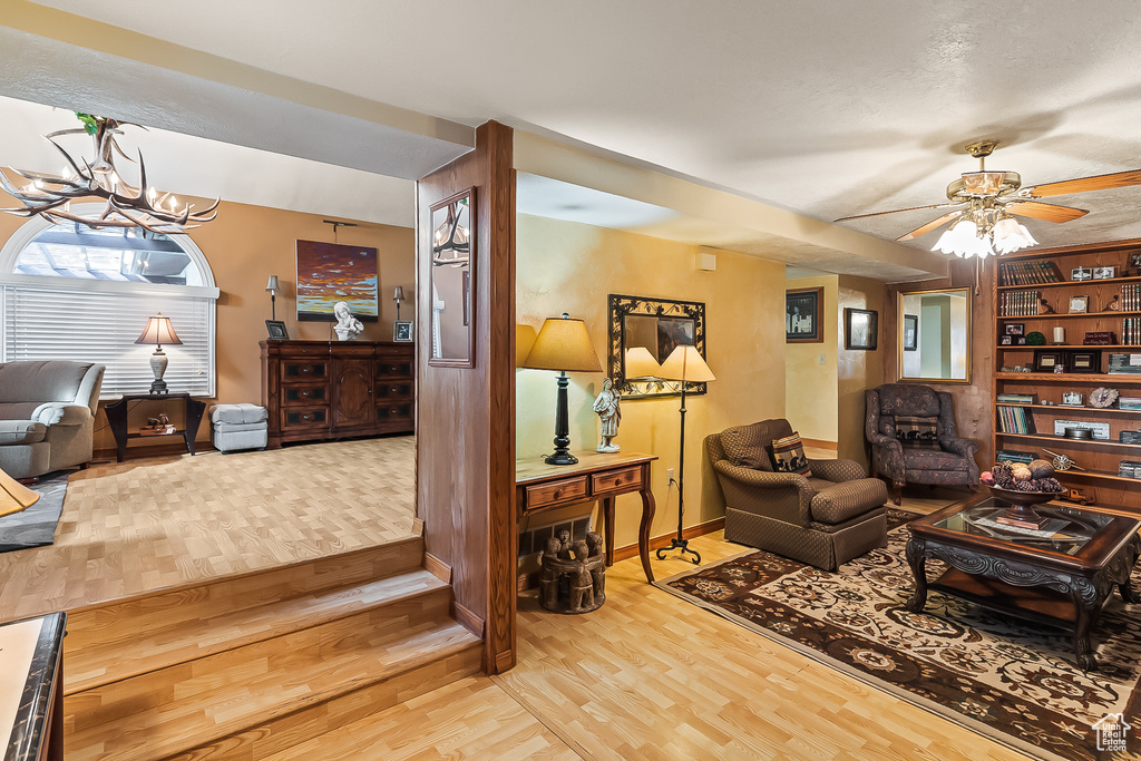 Living area with light wood-style flooring, a chandelier, baseboards, and a ceiling fan