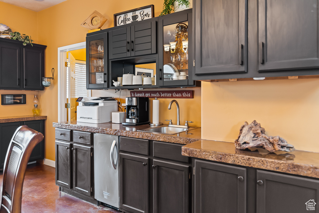 Kitchen featuring a sink, finished concrete floors, glass insert cabinets, and dark countertops