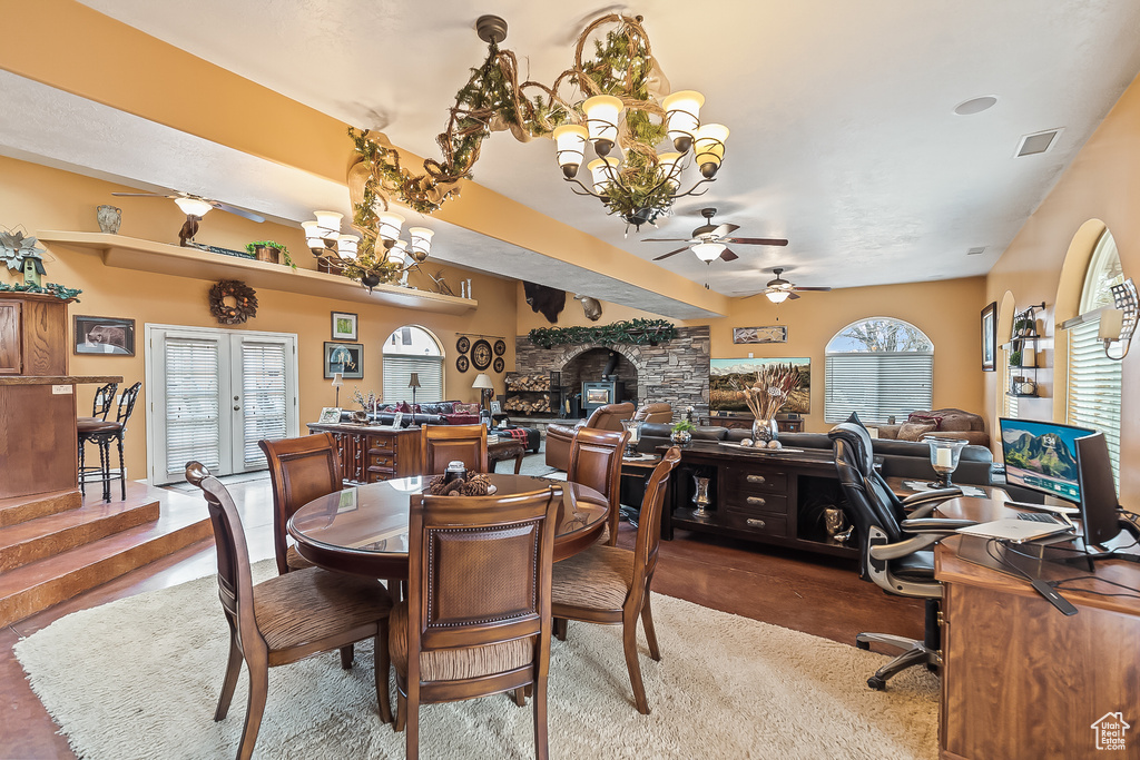 Dining space with ceiling fan, a chandelier, a desk, a stone fireplace, and dark carpet