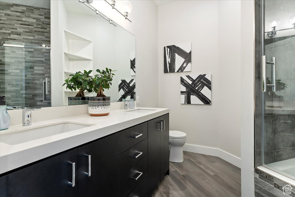 Full bath with a shower stall, baseboards, double vanity, wood finished floors, and toilet