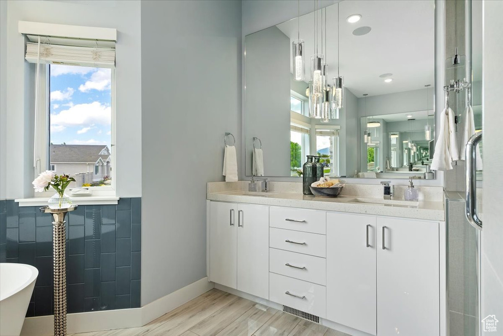 Full bathroom featuring healthy amount of natural light, double vanity, baseboards, a soaking tub, and recessed lighting