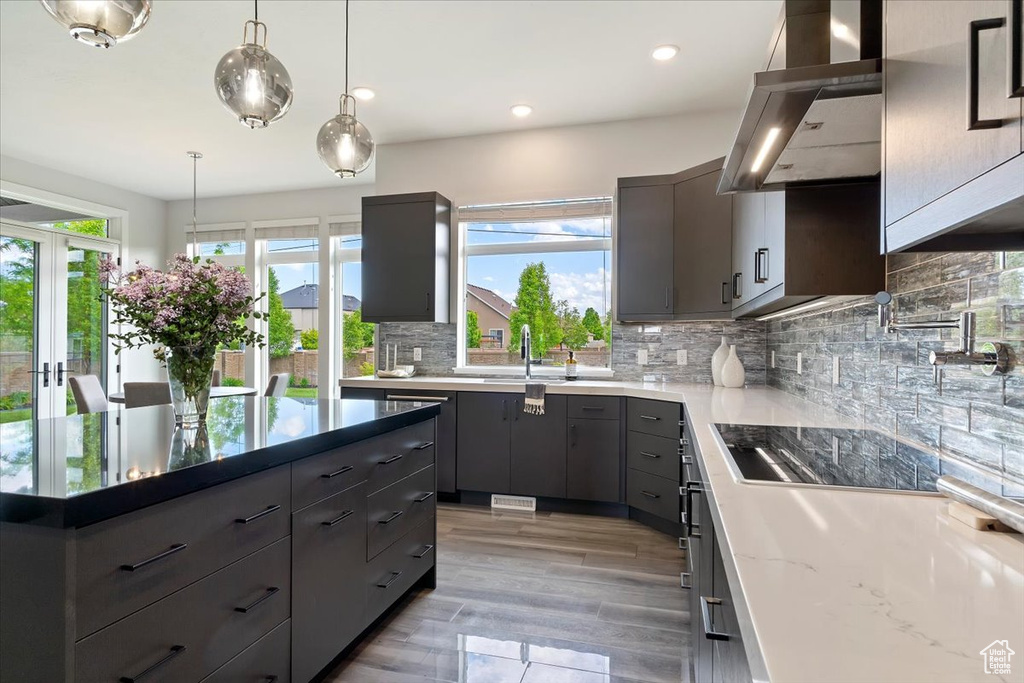 Kitchen featuring wall chimney range hood, a sink, backsplash, gray cabinets, and decorative light fixtures