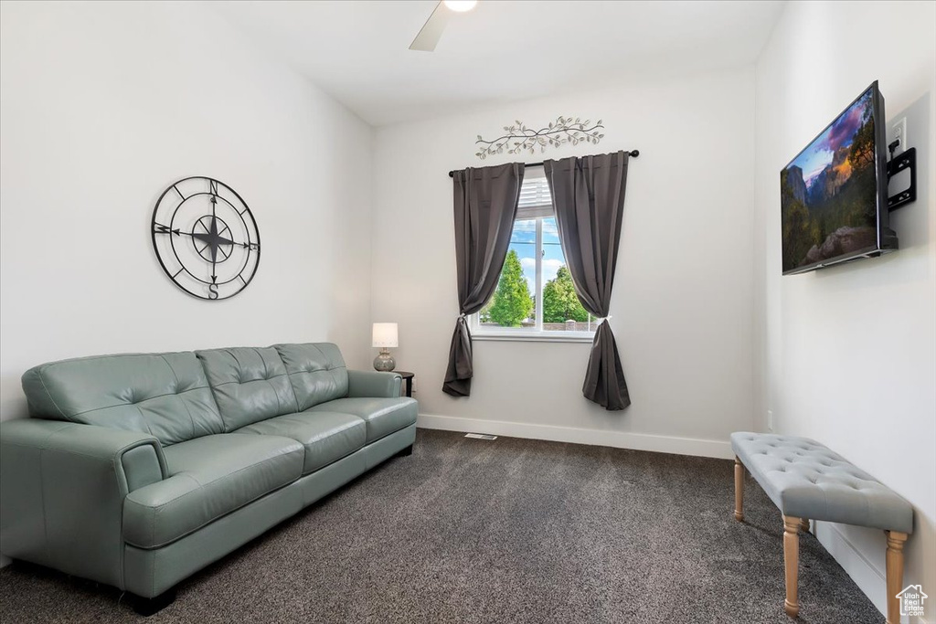 Living room with dark carpet, baseboards, and ceiling fan