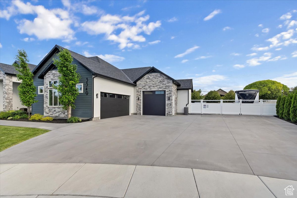 View of front of property featuring stone siding, an attached garage, concrete driveway, and a gate