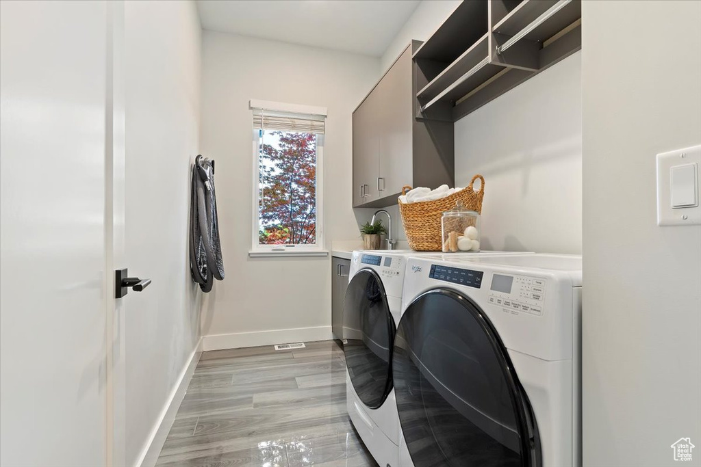 Washroom with washing machine and dryer, cabinet space, baseboards, and light wood finished floors