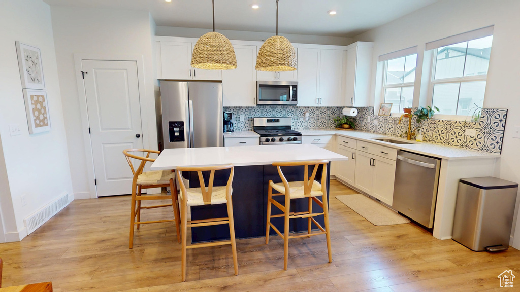 Kitchen with stainless steel appliances, a sink, backsplash, a kitchen bar, and white cabinetry