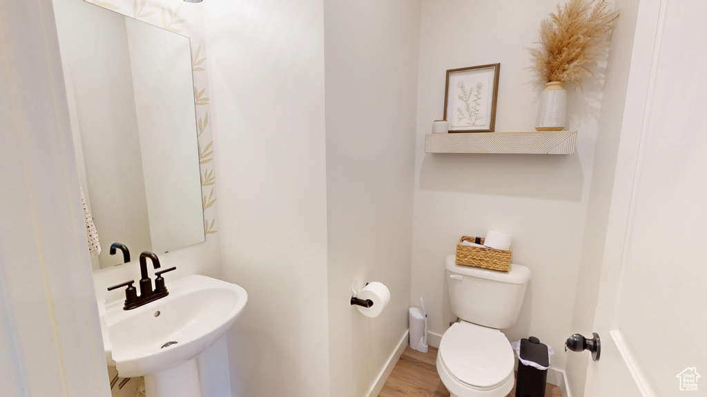 Half bath featuring a sink, toilet, baseboards, and wood finished floors