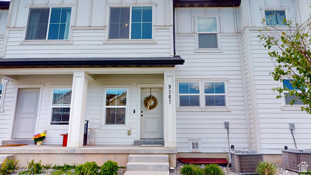 View of exterior entry featuring central AC unit, a porch, and board and batten siding