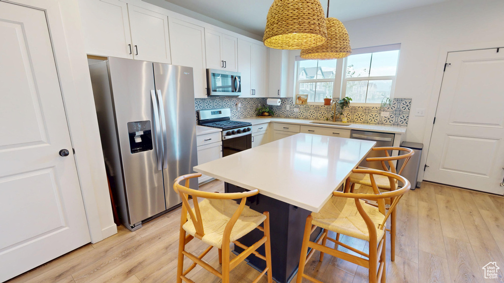 Kitchen featuring stainless steel appliances, light wood-style flooring, a breakfast bar, and decorative backsplash
