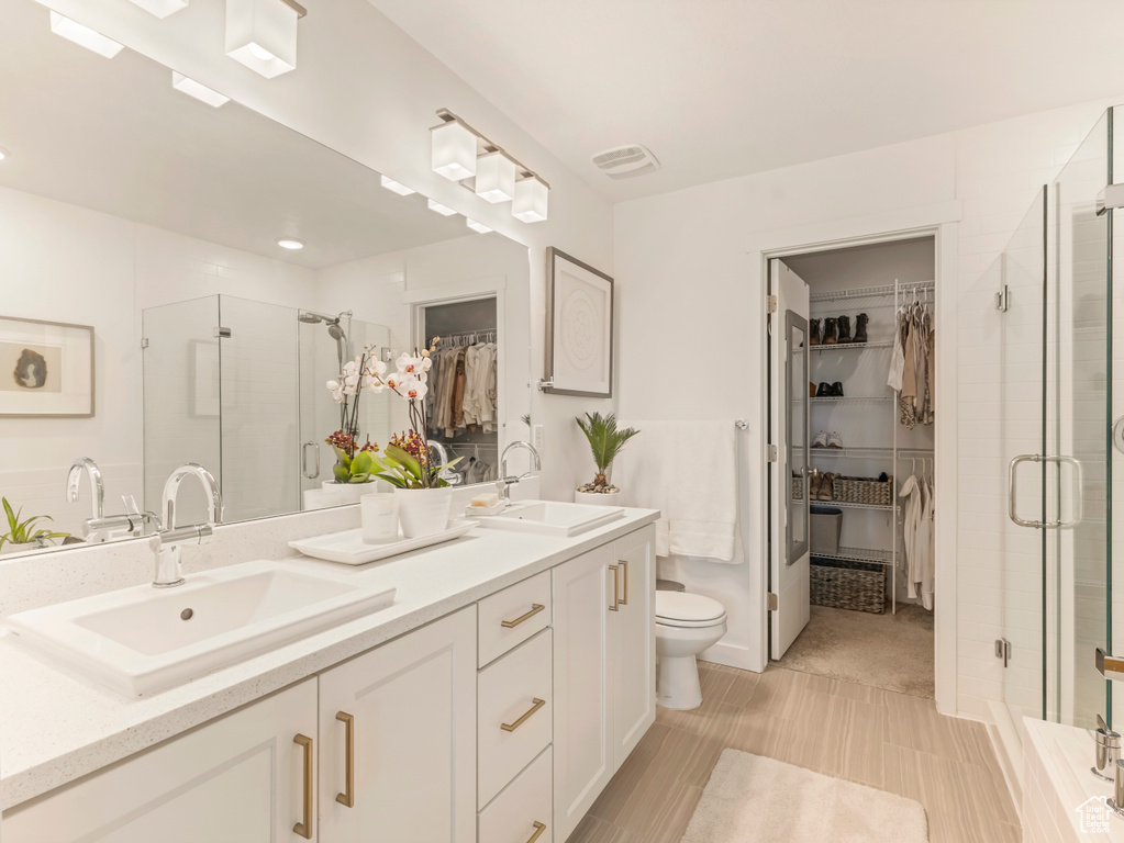 Bathroom with a stall shower, a walk in closet, double vanity, and toilet