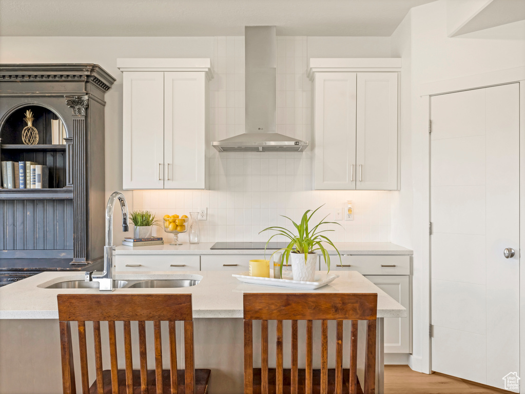 Kitchen featuring wall chimney range hood, a sink, white cabinetry, and light countertops