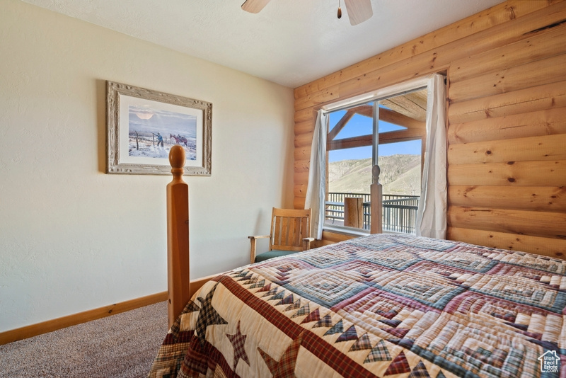 Carpeted bedroom with rustic walls, access to exterior, baseboards, and ceiling fan
