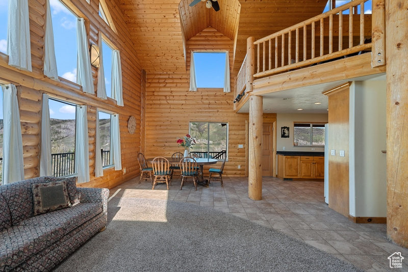 Living area with high vaulted ceiling, log walls, wooden ceiling, baseboards, and a ceiling fan