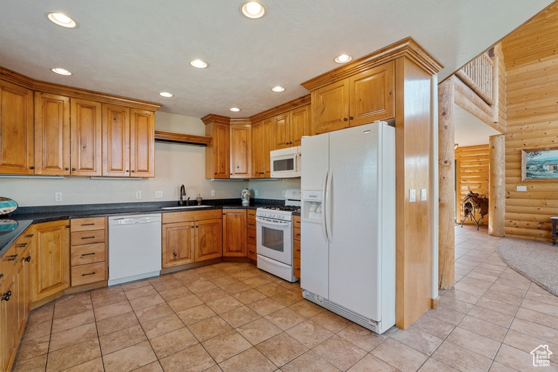 Kitchen with white appliances, rustic walls, a sink, dark countertops, and recessed lighting