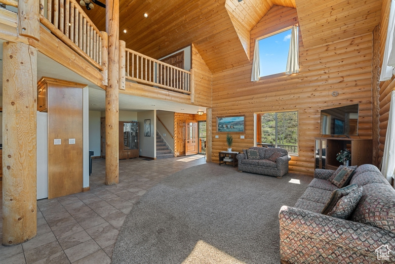 Living room featuring high vaulted ceiling, wood ceiling, stairway, and log walls