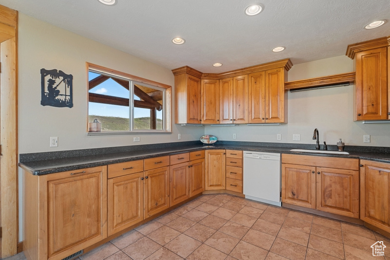 Kitchen featuring a sink, dishwasher, recessed lighting, dark countertops, and brown cabinetry