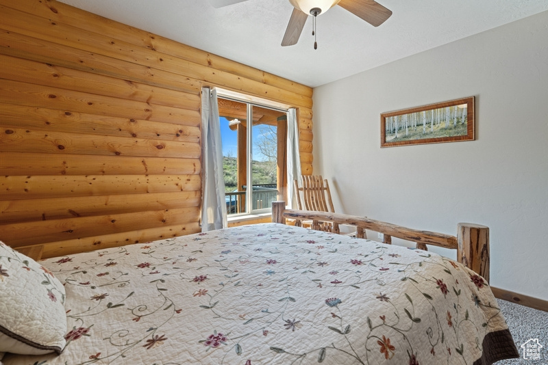 Carpeted bedroom featuring rustic walls, baseboards, access to outside, and a ceiling fan