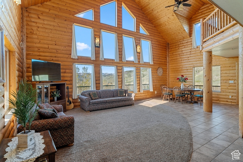Living room with high vaulted ceiling, log walls, plenty of natural light, ceiling fan, and wooden ceiling