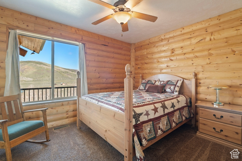 Bedroom featuring log walls, dark carpet, access to outside, a mountain view, and ceiling fan