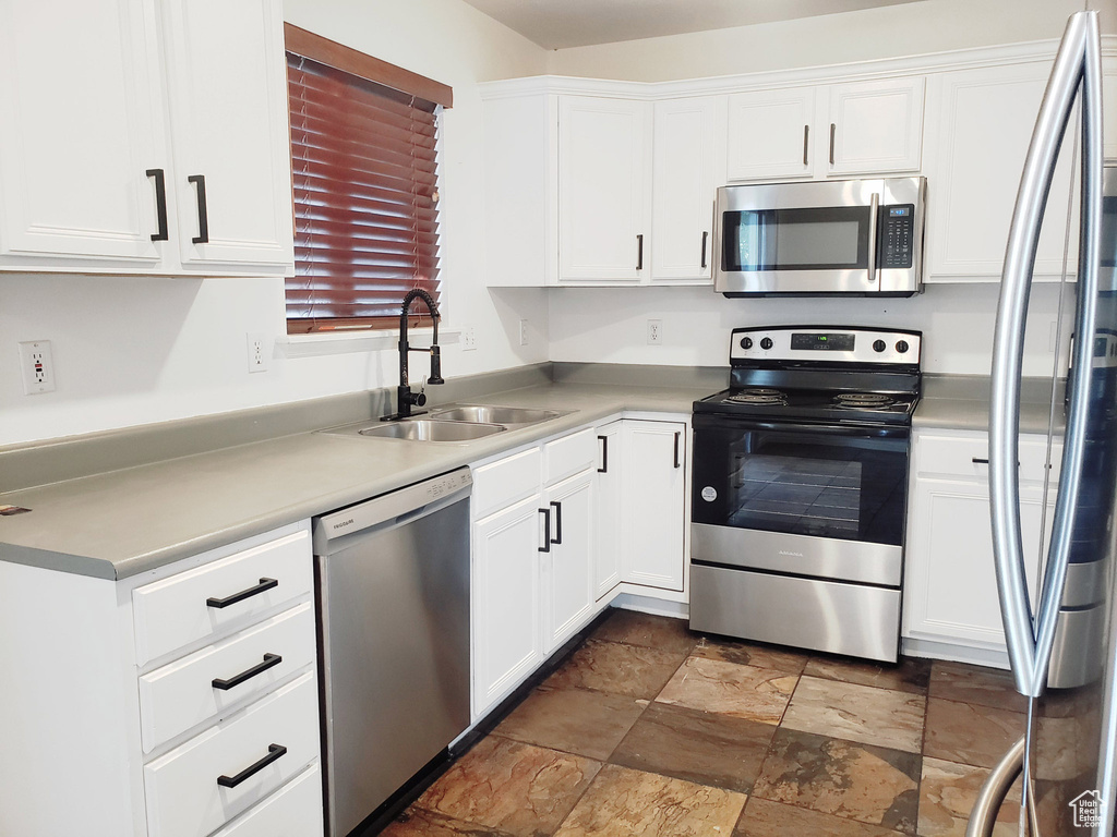 Kitchen with stainless steel appliances, a sink, dark stone finish flooring, white cabinets, and light countertops