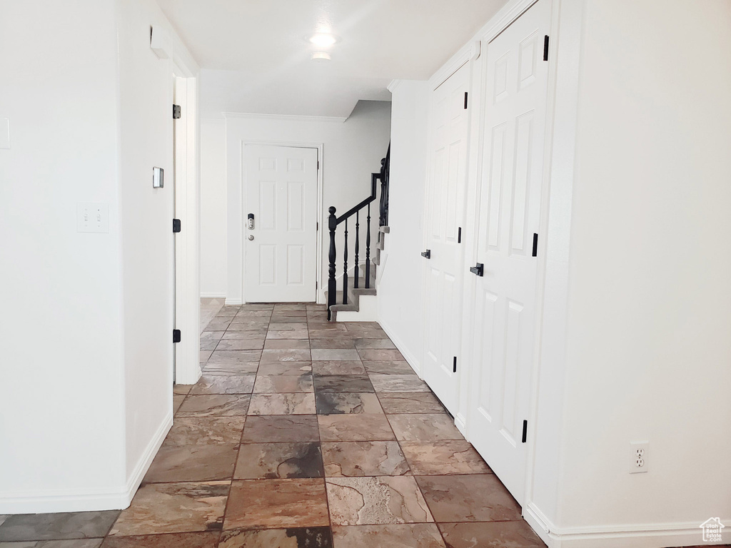 Hallway with baseboards, stone tile floors, and stairs