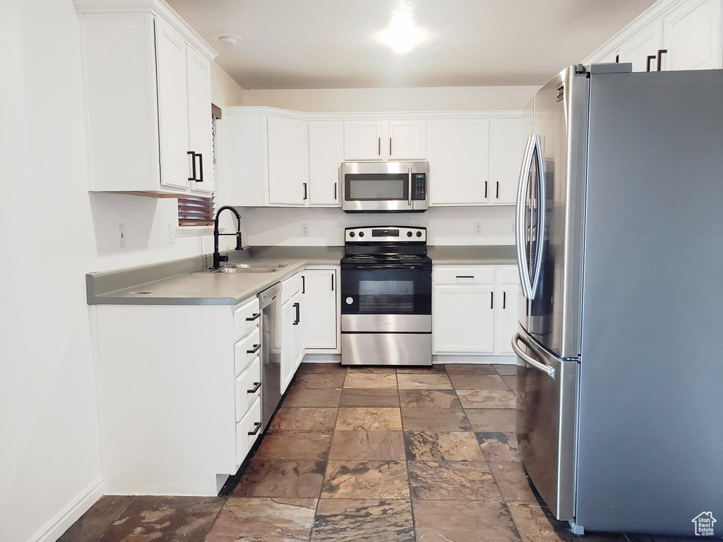 Kitchen with stainless steel appliances, a sink, stone tile flooring, white cabinetry, and light countertops
