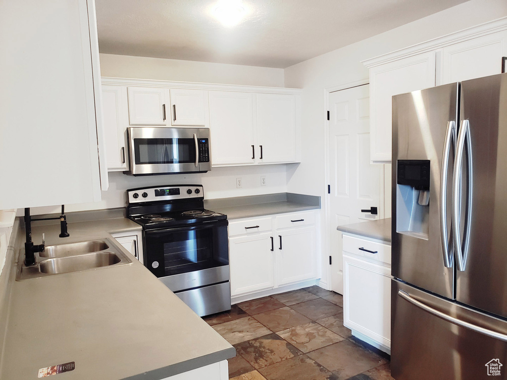 Kitchen featuring stainless steel appliances, a sink, white cabinets, light countertops, and dark stone finish flooring