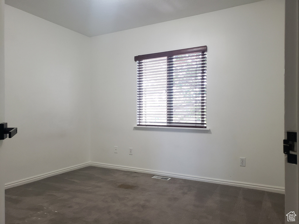 Unfurnished room featuring baseboards and dark carpet