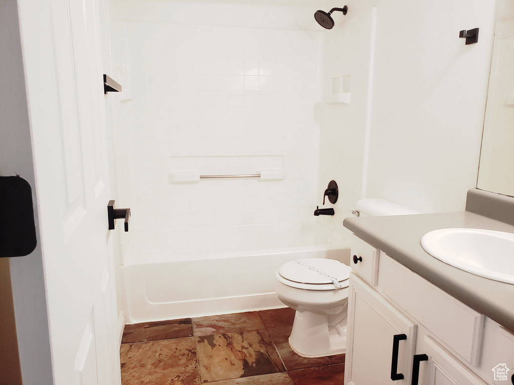 Full bath with stone finish flooring, toilet, vanity, and shower / bath combination